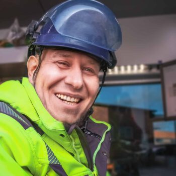 lächelnder Servicetechniker mit blauem Helm und grün-gelber Warnjacke